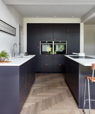 sleek, contemporary kitchen with dark cabinetry contrasted by minimalist white worktops. The handleless design features playful pops of colour with bold orange circular accents on the cupboard doors.