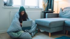 Woman wrapped in duvet sitting on floor next to radiator