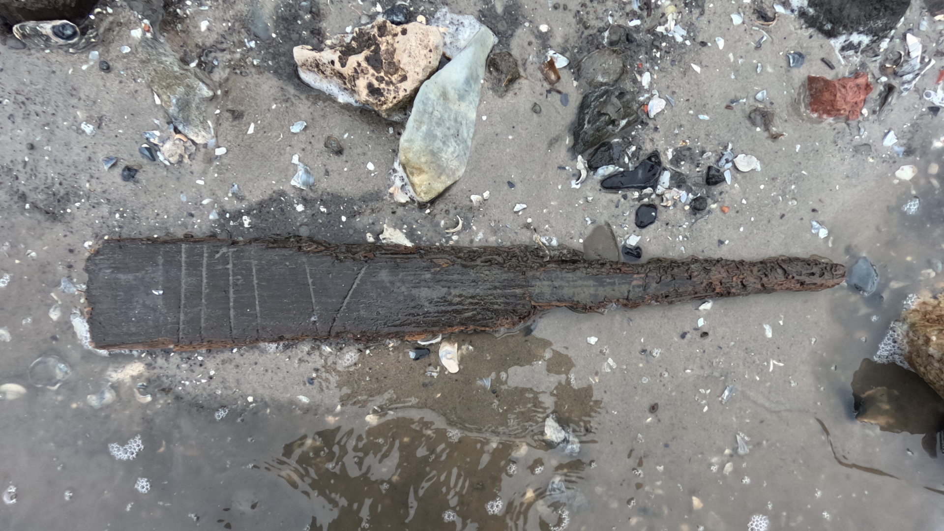 a tapering piece of wood with Roman numerals on a beach
