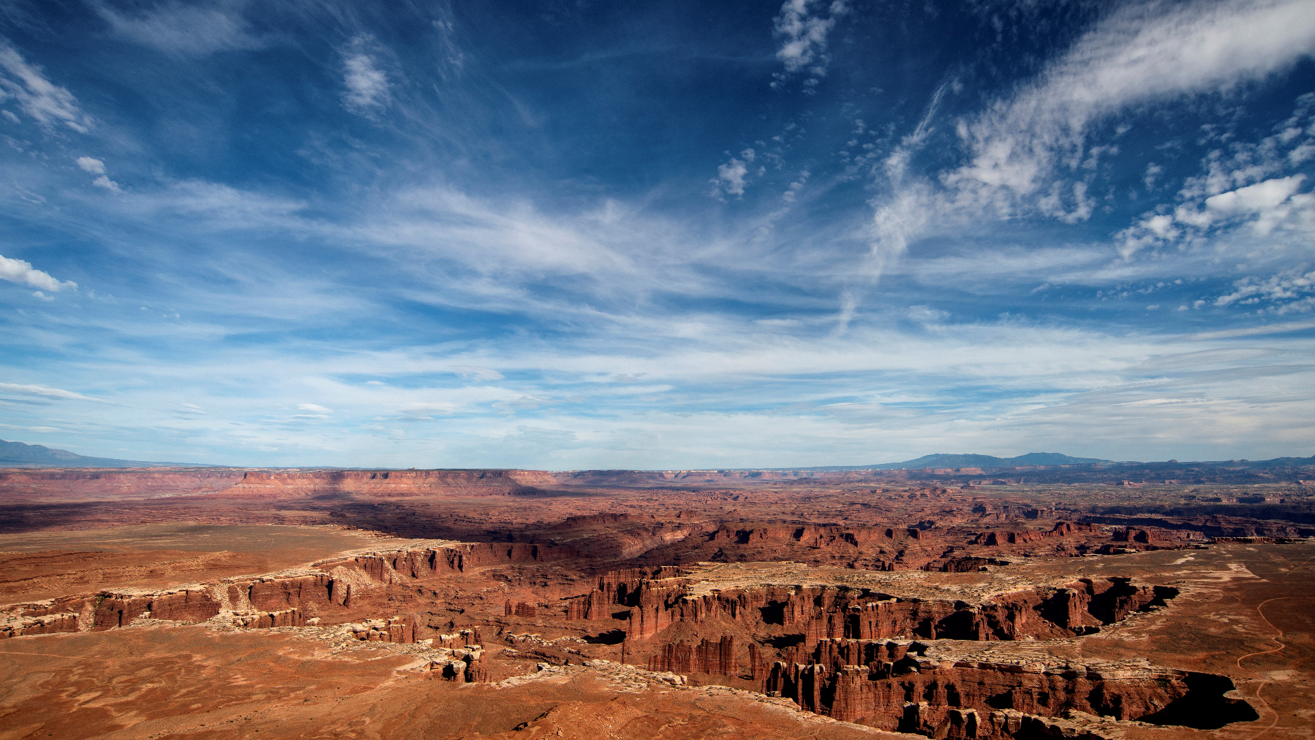red rock structures and canyons below a blue sky with wispy white clouds.