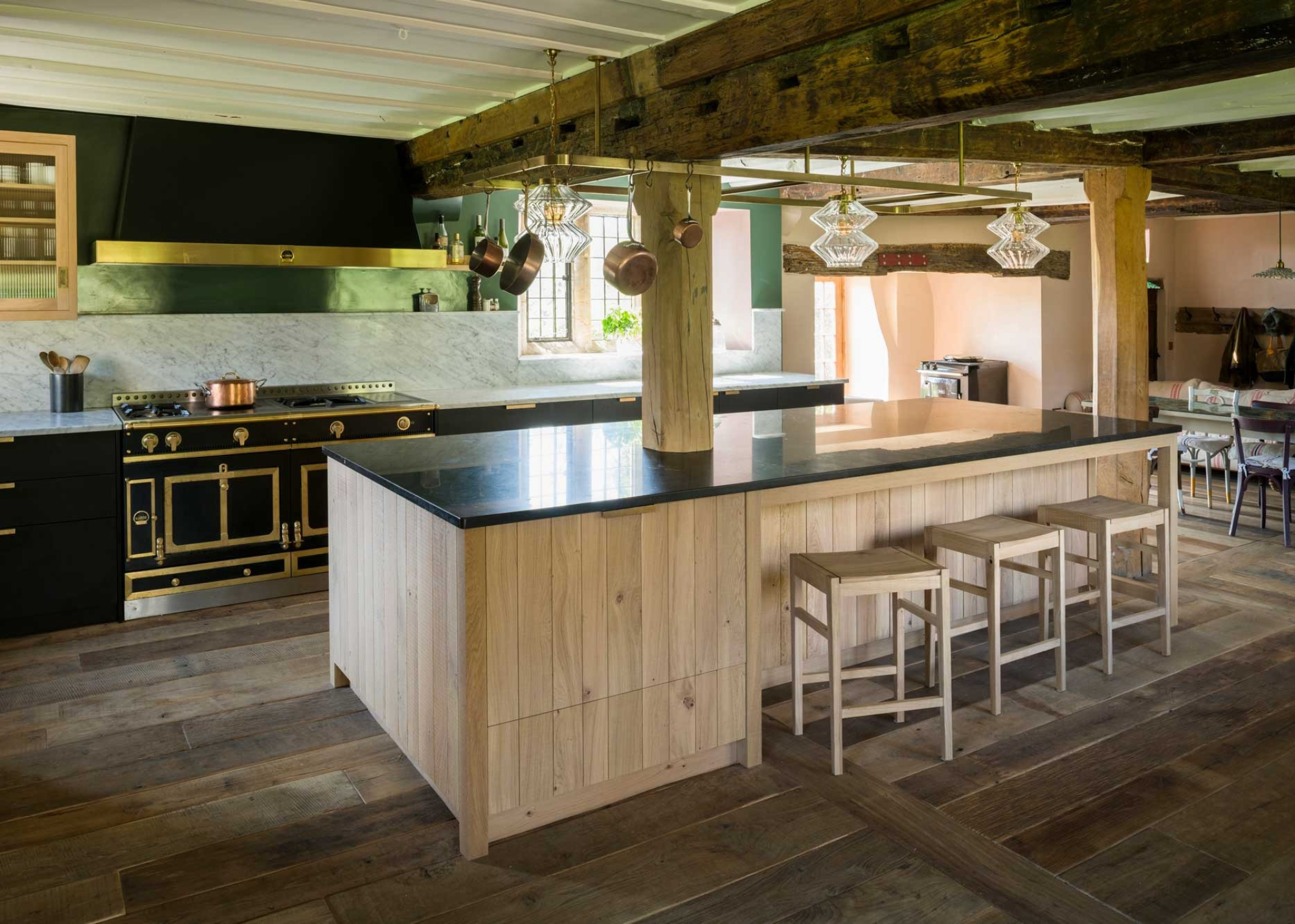 rustic kitchen with large wooden island with bar seating, built around a timber pillar. A black la cornue range cooker sits opposite the island