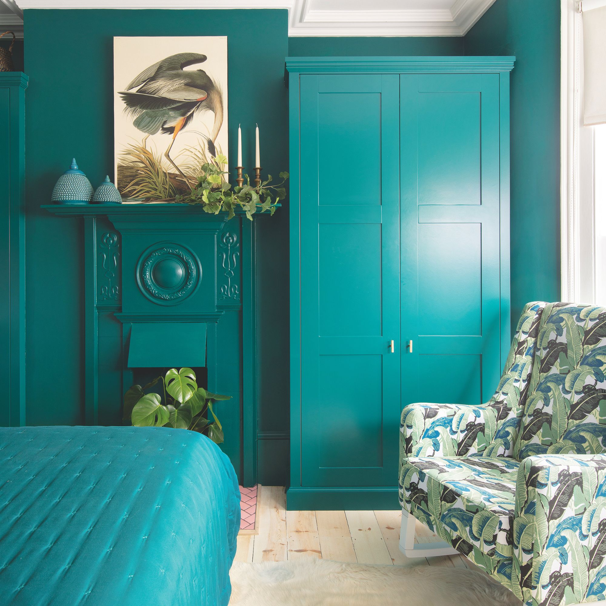 Teal colour drenched bedroom with teal wardrobes, teal bedding and an accent chair with palm leaf print
