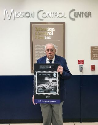 Veteran NASA director George Abbey poses with an enlargement of one of the Isle of Man's 2019 "One Small Step" postage stamps at the Mission Control Center in Houston.