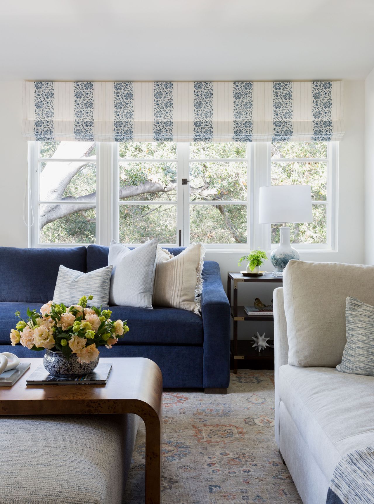 family living room with white and blue modular sofas and white footstool with wooden coffee table section oriental rug and striped roman blinds