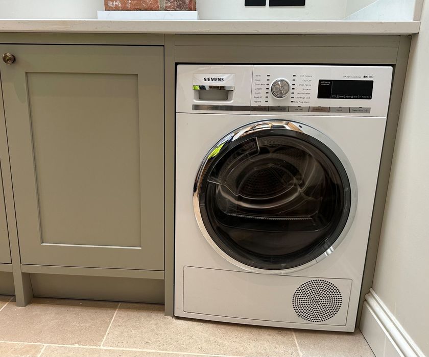 A Siemens tumble dryer in a utility room with green cupboards