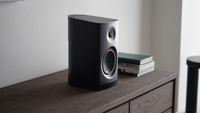A black Yamaha NX-70A wireless speaker on a wooden cabinet next to a pile of books.