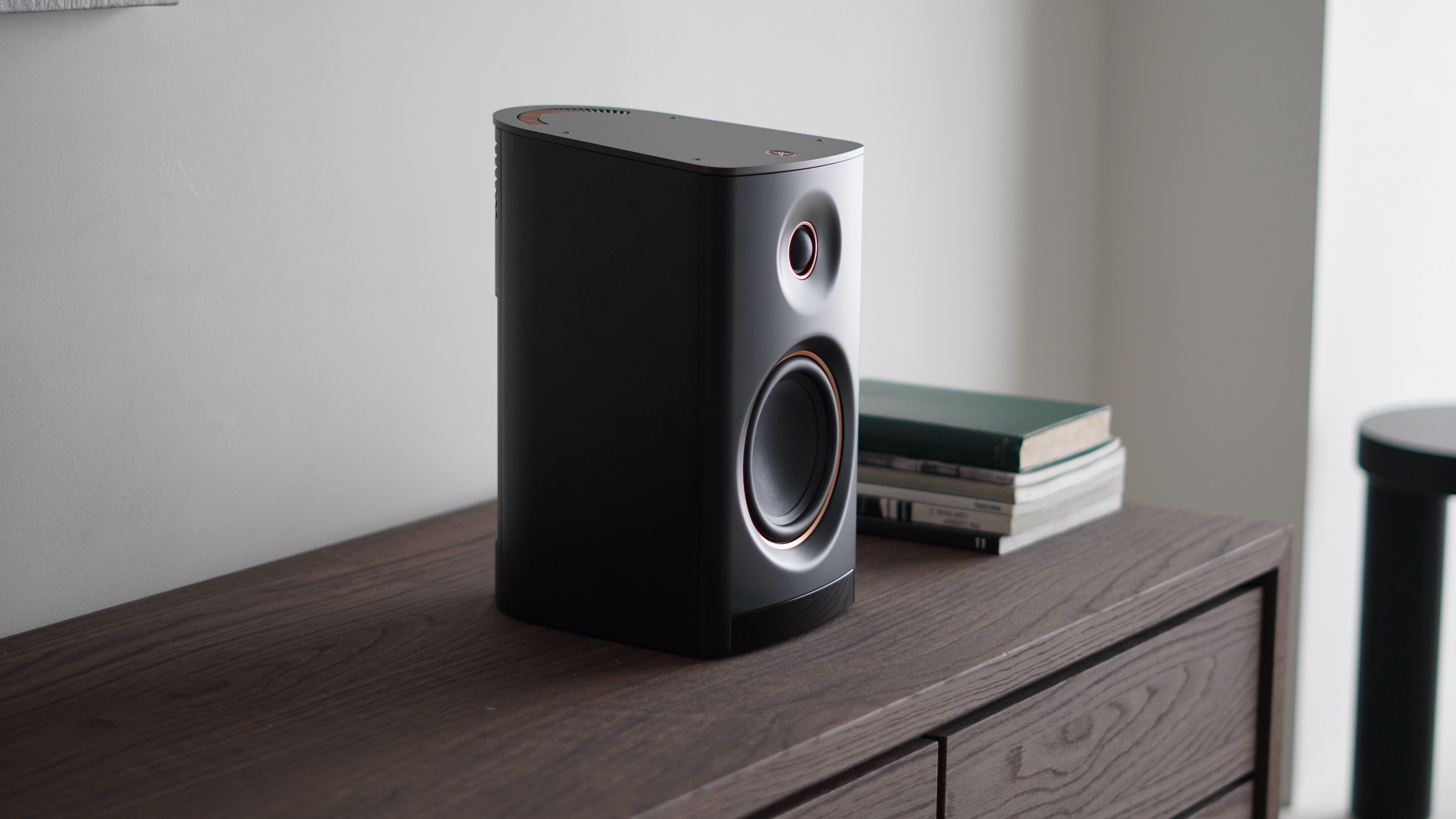A black Yamaha NX-70A wireless speaker on a wooden cabinet next to a pile of books.