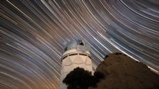 A long exposure photo shows the series of white star streaks across the night sky above a circular observatory.