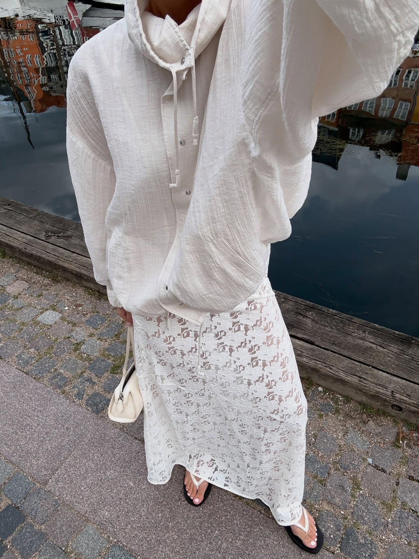 Woman wears white technical jacket, lace skirt, flip flops