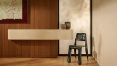 Image of a minimalist entryway that has beige walls, wood floors, and the back wall is wood paneled. There is a large white marble shelf attached to the wall and a metal chair to the right of the shelf.