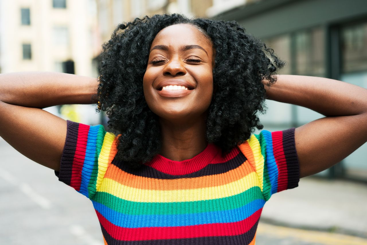 a happy woman smiling and touching her hair, to illustrate our curly hairstyles guide