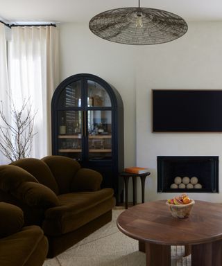 A living room with green velvet armchairs, a black arched cabinet and a circular wooden coffee table