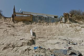 A home on the beach installing its own defences against coastal erosion with a metal sheet and small barricade against the cliff edge