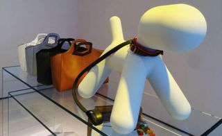 Glass server with display of handbags next to an ornament looking like a dog with a leather strap around its neck