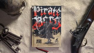 Pirate Borg book on a sandy surface with keys, a skull, and a flintlock pistol nearby