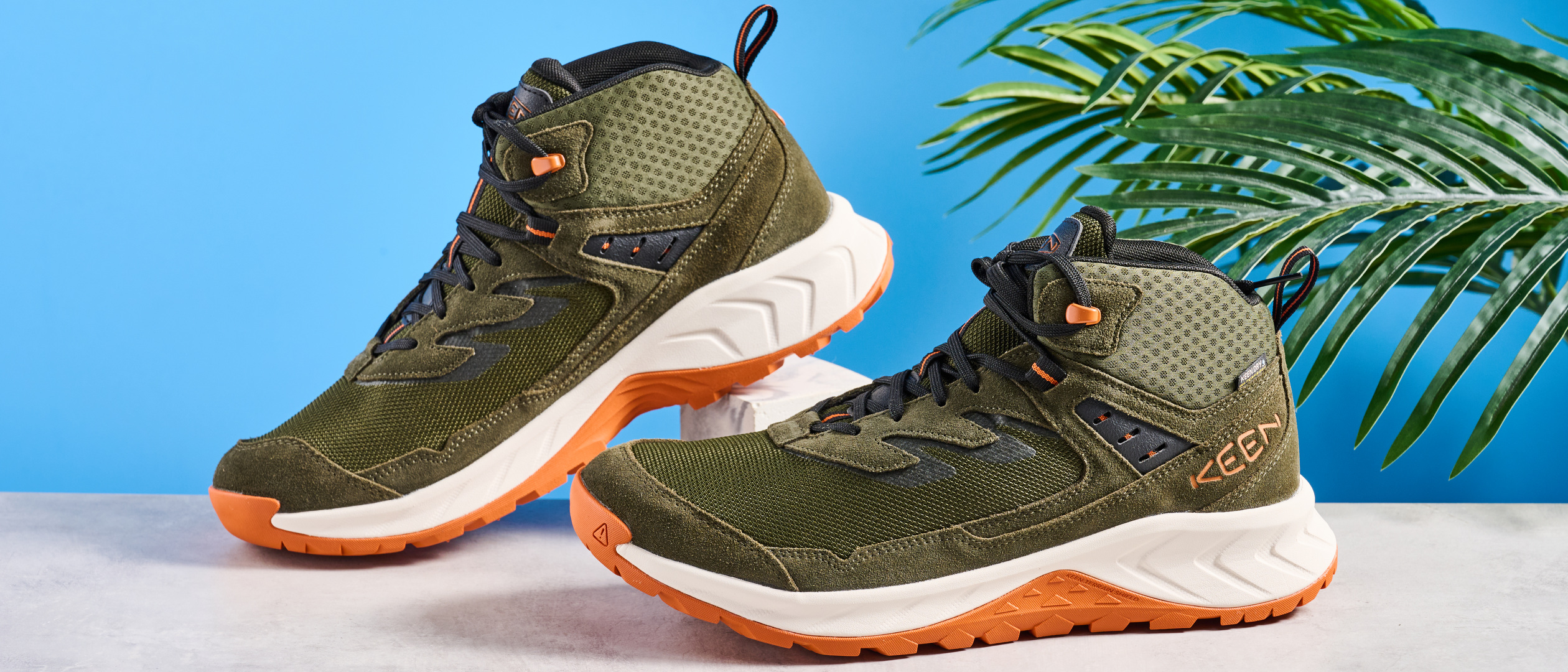 The Keen Hightrail Mid boots in Green on a stone surface against a blue background