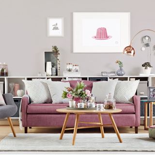 grey living room with a long white open chest drawer topped with accessories and a pink sofa with neutral colored pillows and a wooden circle coffee table with floral accessories