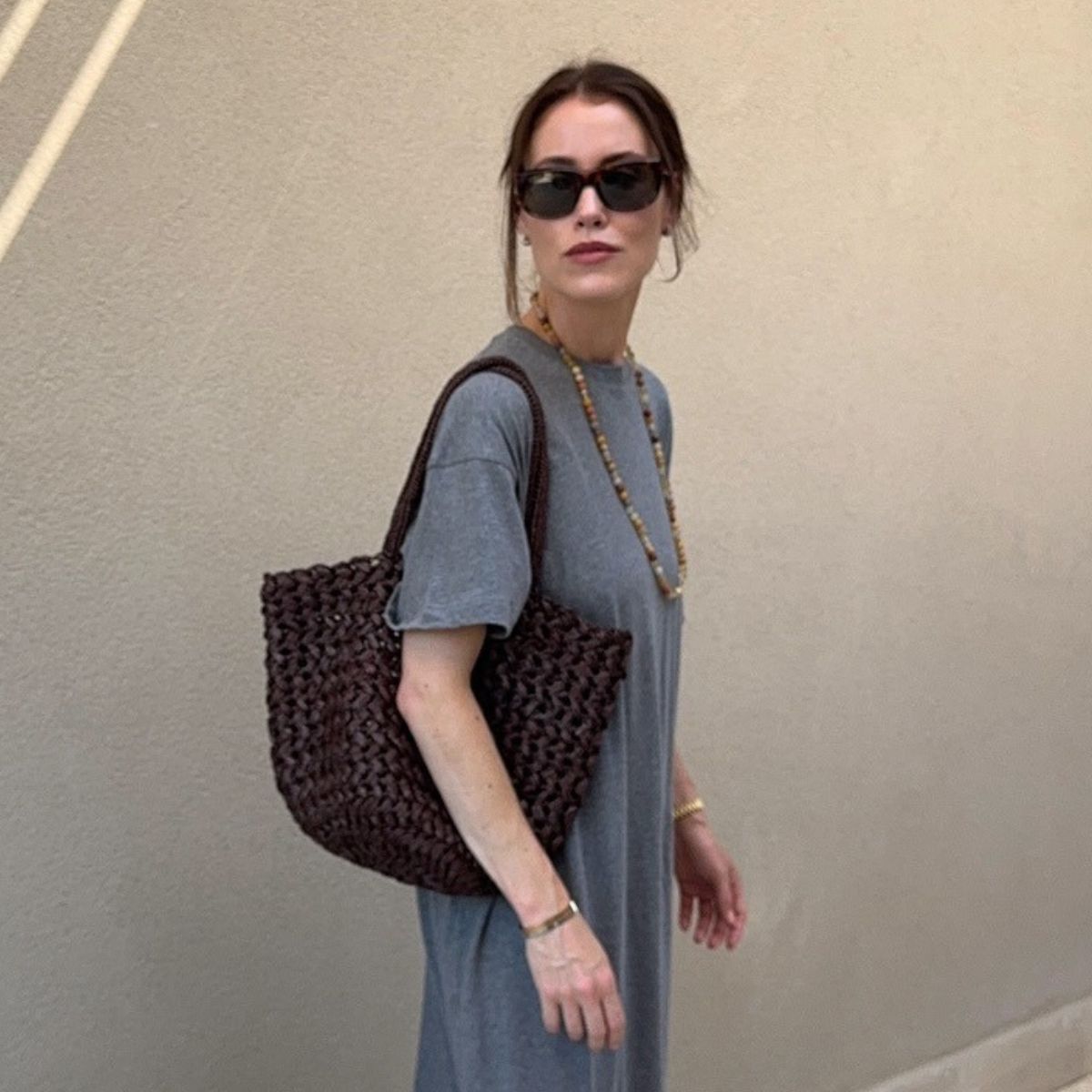 Woman wears grey dress, bead necklace and brown woven bag