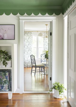 A view of a dining room through a doorway with white walls and a green ceiling with scalloped detailing