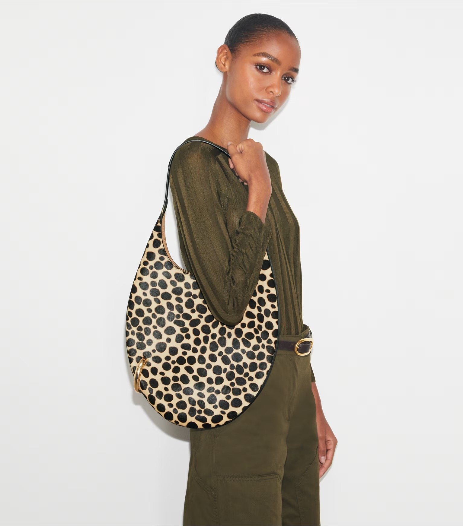 A model holding an animal-print oval shoulder bag featuring a gold piercing-like ring.