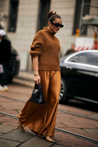 Woman walking the street in an orange turtleneck sweater, slip skirt, and heels