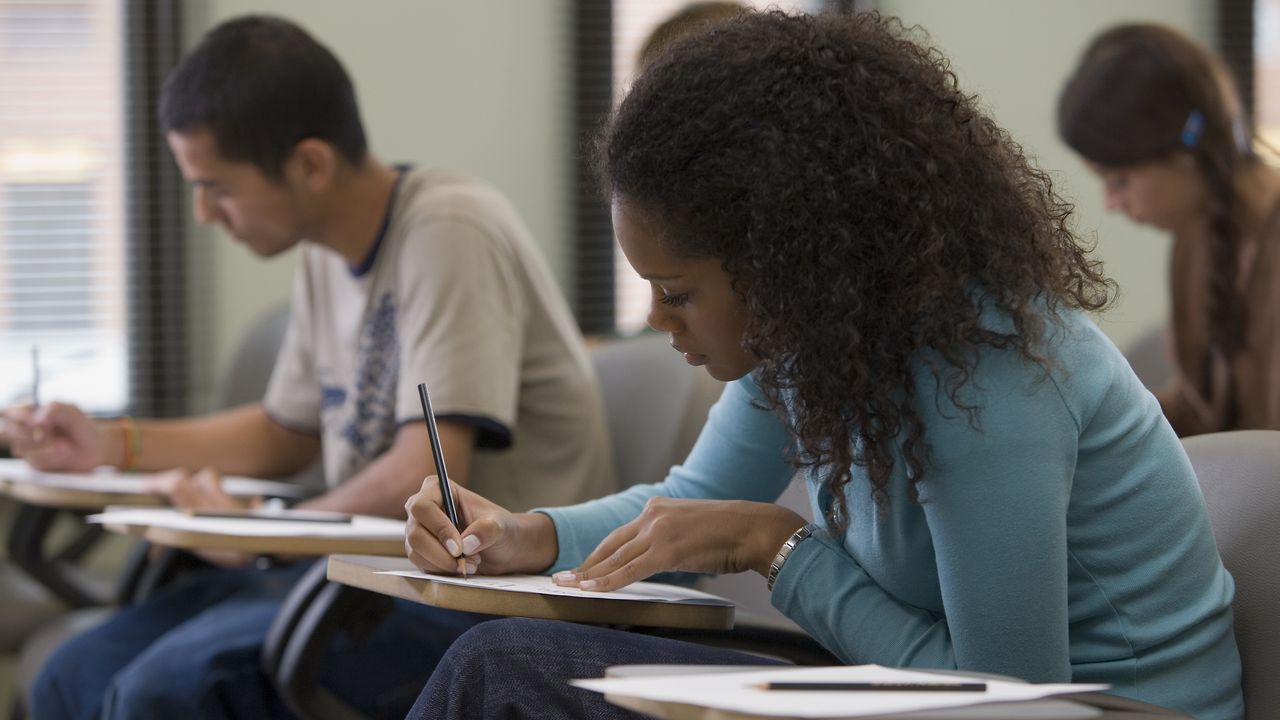 Young adults take a test while sitting at desks in a classroom.