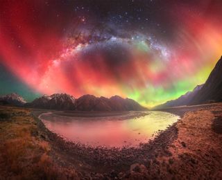 A photograph of the red northern lights and Milky Way over a lake and mountains