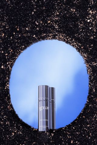 Volcanic rock background, Ignae vegan skincare bottle in front of a blue mirrored disk