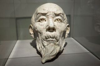 A statue of a face for an older man with a mid-long beard. Red dots covers the face.
