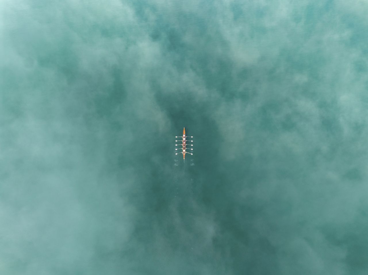 An aerial view of a rowing team gliding through the pristine waters of Lake Zurich in Switzerland. The team is perfectly synchronized, with oars cutting cleanly into the turquoise, misty surface