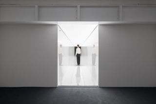 Man in white corridor with white LED light designed by Ryoji Ikeda