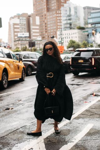 Jasmine Fox Suliaman in a black dress, black flats, a gold belt in the street at New York Fashion Week.