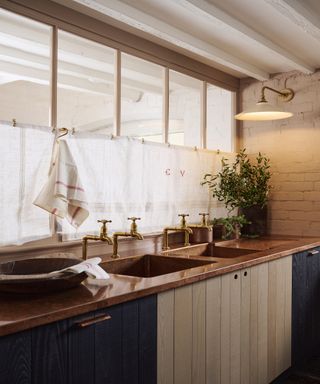 Shiny copper kitchen counter with classic gold taps, linen window treatments and mid century conical cream wall sconce