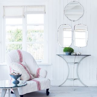 white wood panelled room with chair covered in French grain sack cloth and vintage wall mirrors