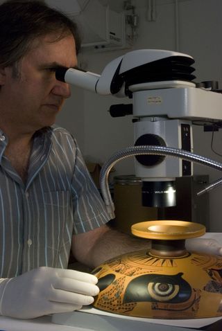 J. Paul Getty Museum Associate Conservator Jeffrey Maish examining an Attic black figure kylix under a binocular stereo-microscope.