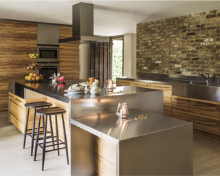 Modern kitchen ideas illustrated by an exposed brick space with handleless wooden cabinetry and metal worktops and breakfast bar.