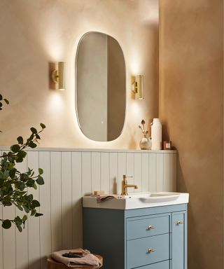 bathroom with wall lights either side of mirror and terracotta walls with blue vanity unit