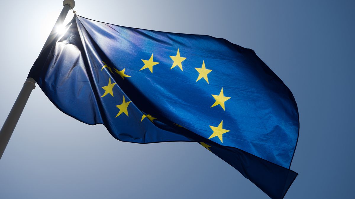 Flag of the European Union (EU) pictured during the day with sunlight behind and blowing in the wind.