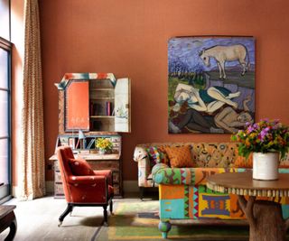 Folk living room with orange walls, surrealist art, vintage dresser, upholstered orange armchair and upholstered patterned sofas