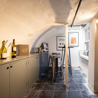 Wine cellar with bar stools and window-seat cushion with wine on top of grey cupboard next to ice bucket