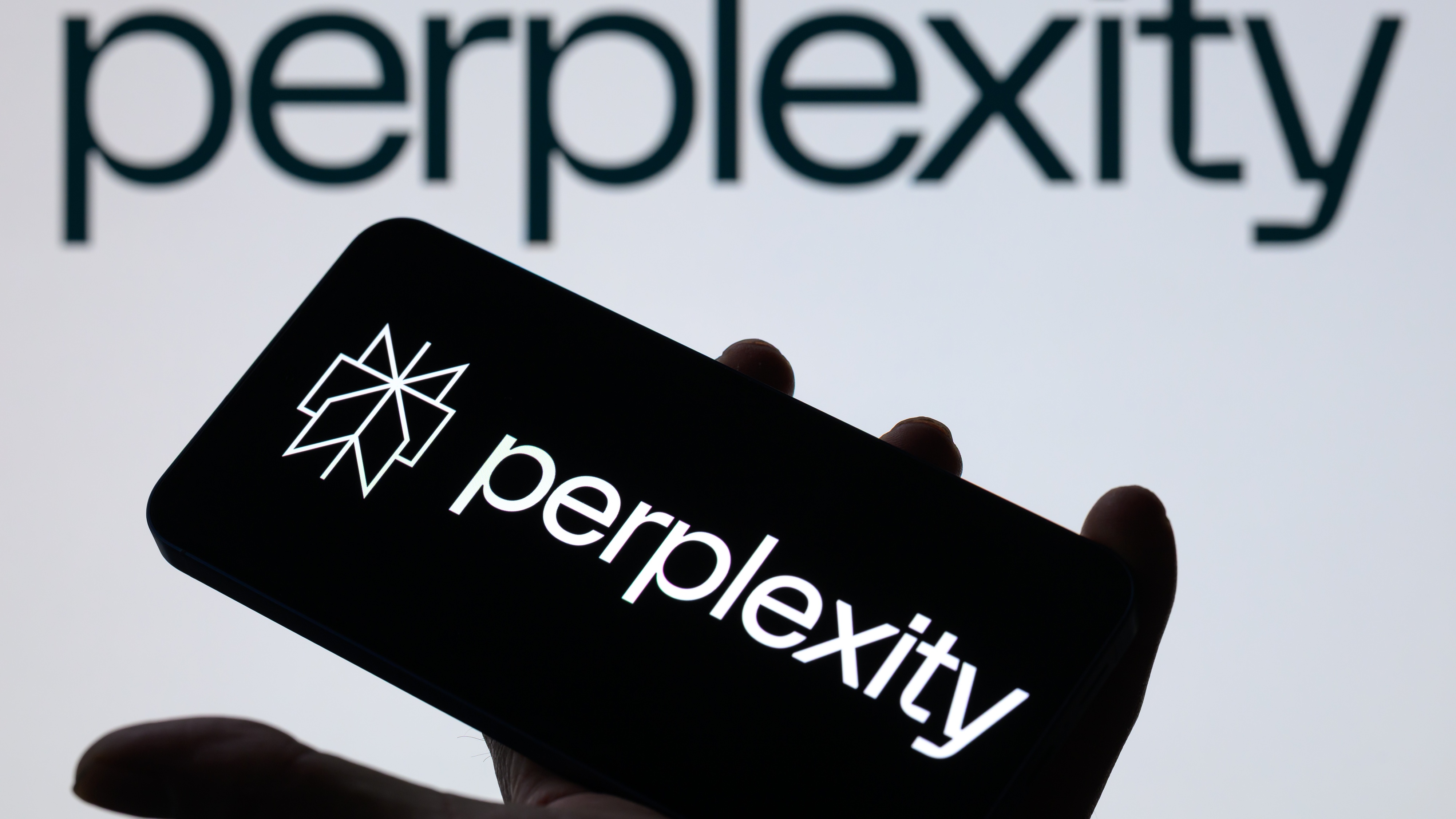 The Perplexity logo is displayed on a mobile phone with Perplexity seen in the background.