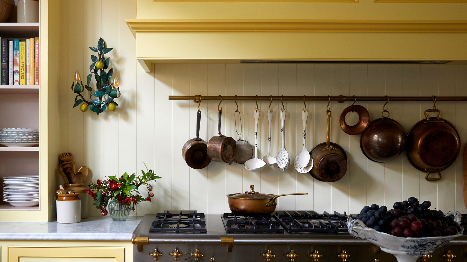 Yellow kitchen with a brass rack with butchers hooks hanging pots and pans