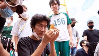 Director Hwang Dong-hyuk inspects a piece of Dalgona Candy on the set of Squid Game. 