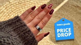 A woman's hand with burgundy nails wearing the silver heritage Oura Ring 3 on index finger with Tom's Guide price drop logo
