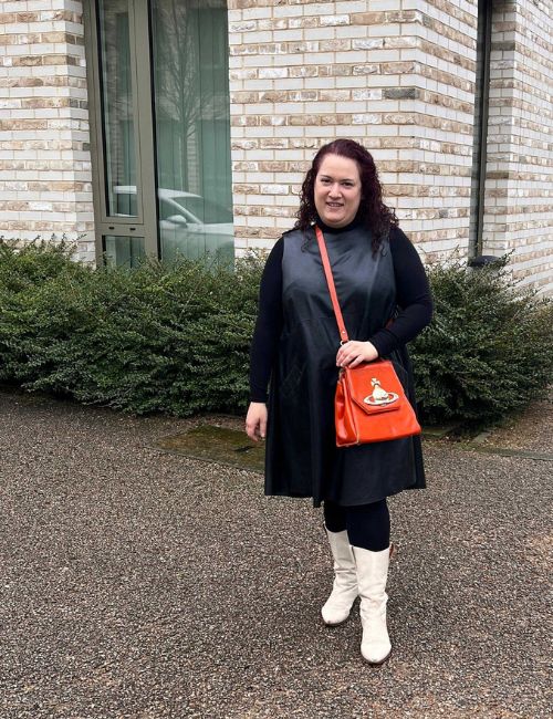 Rivkie wearing a black dress and orange handbag