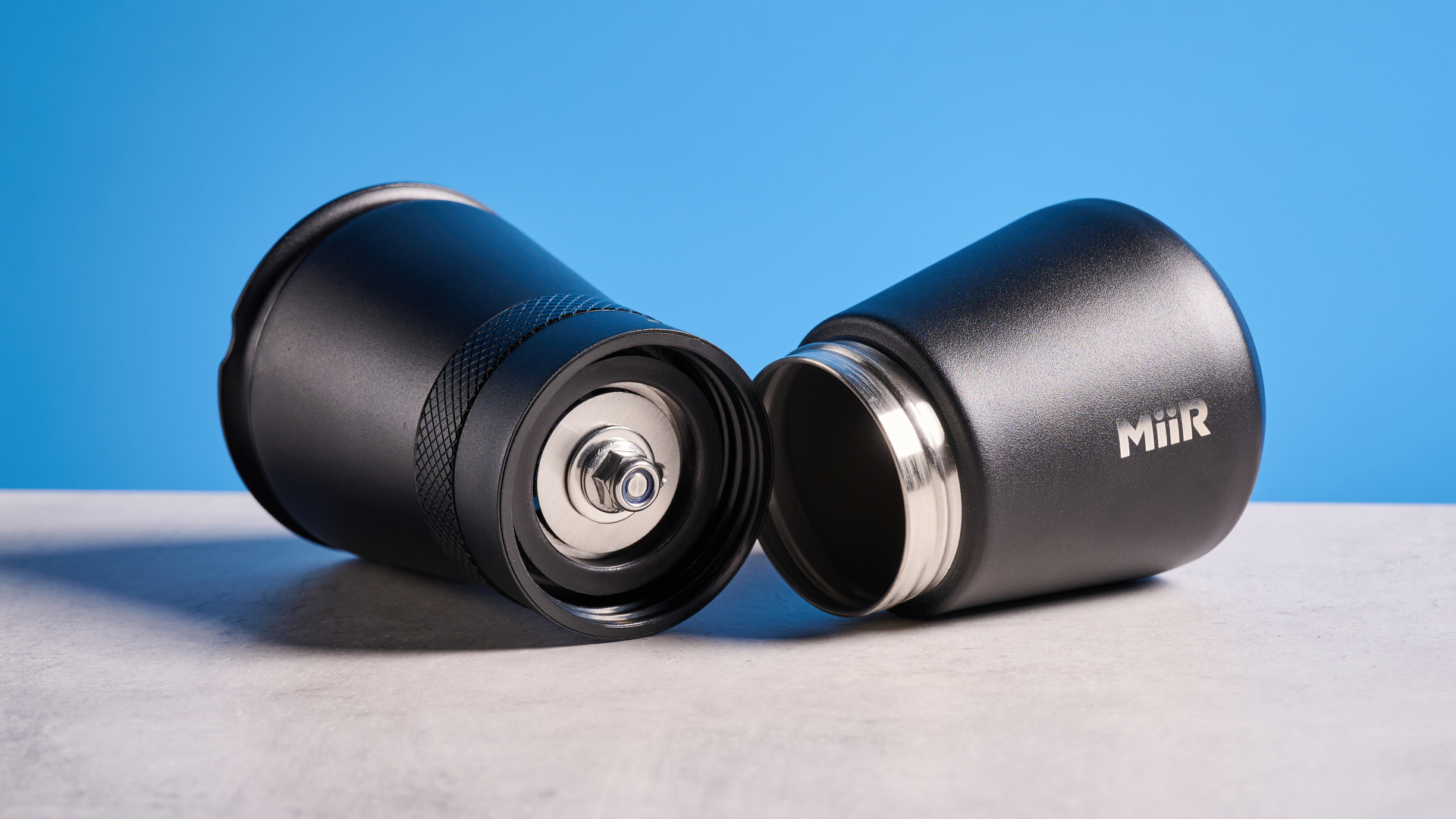 MiiR New Standard Hand Grinder in matte black photographed in front of a blue background