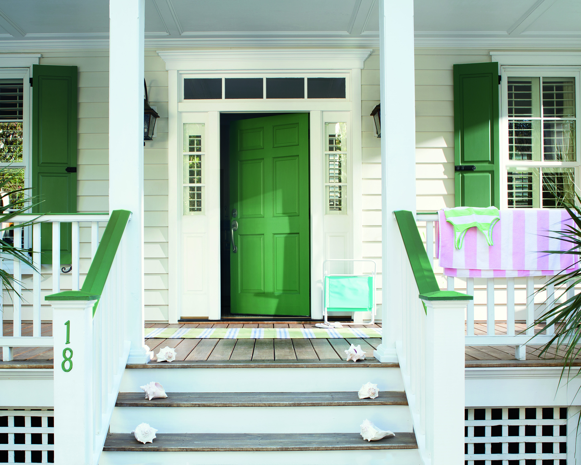 House exterior with decking on stairs, green front door and green shutter window treatment with striped pink and white beach towel