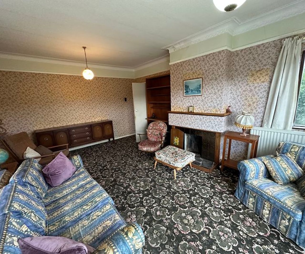 An old fashioned living room with a small fireplace with a floor to ceiling window