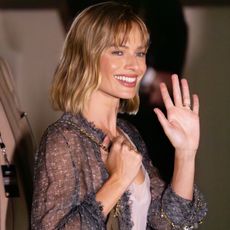 Margot Robbie attending the Chanel F/W 26 show during PFW, wearing a sheer jacket, tank, and pants with pumps and a Chanel 25 mini bag