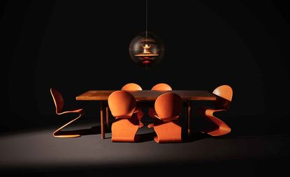 A dark room featuring furniture by Verner Panton, including orange S-shaped chairs and a VP Globe pendant lamp
